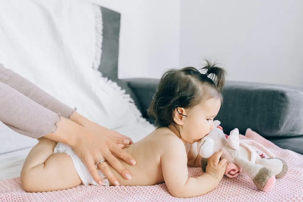 Ein Baby liegt auf einer rosa Decke, eine Hand massiert seinen Rücken.