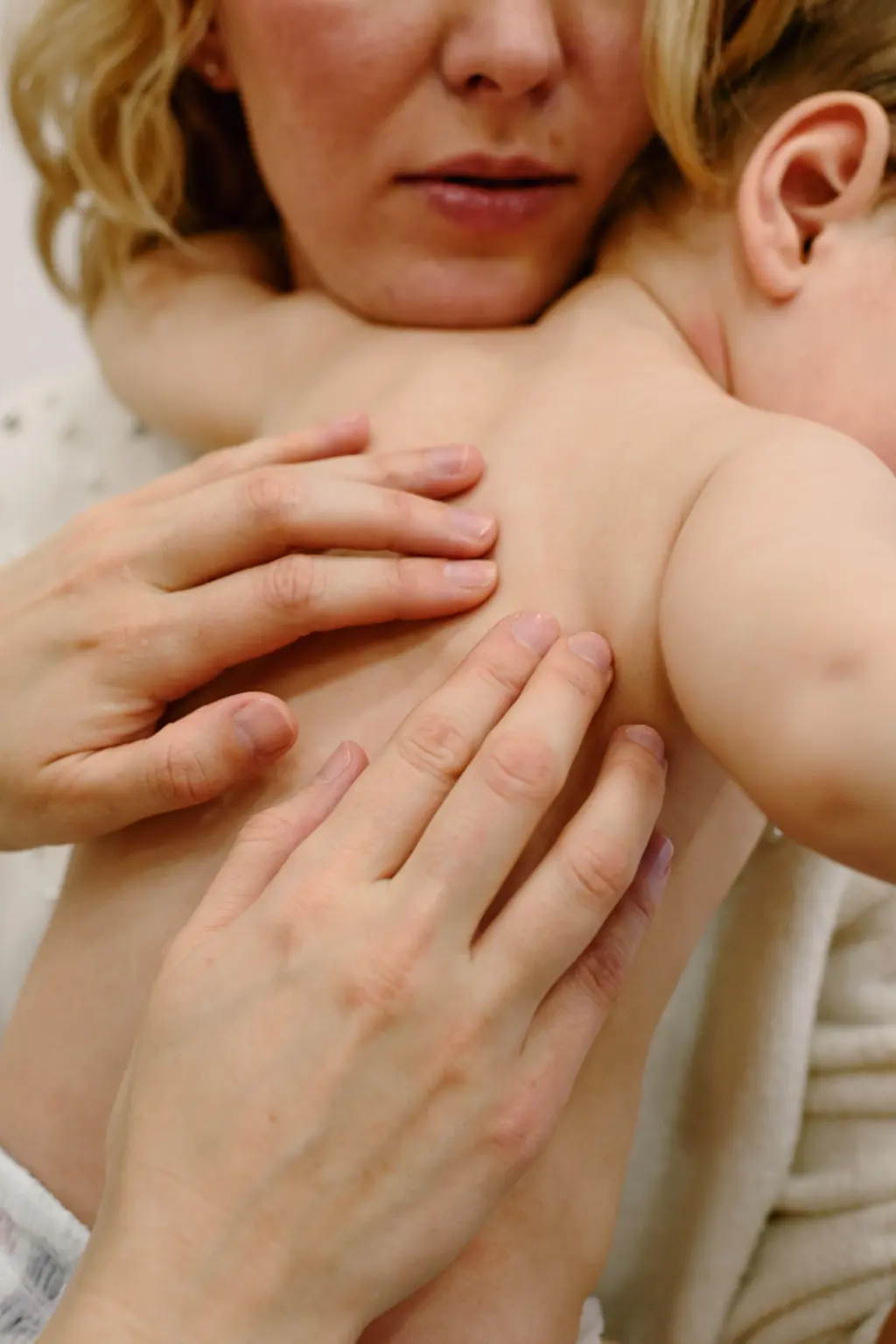 Eine Mutter legt ihre Hände sanft auf den Rücken ihres Babys.